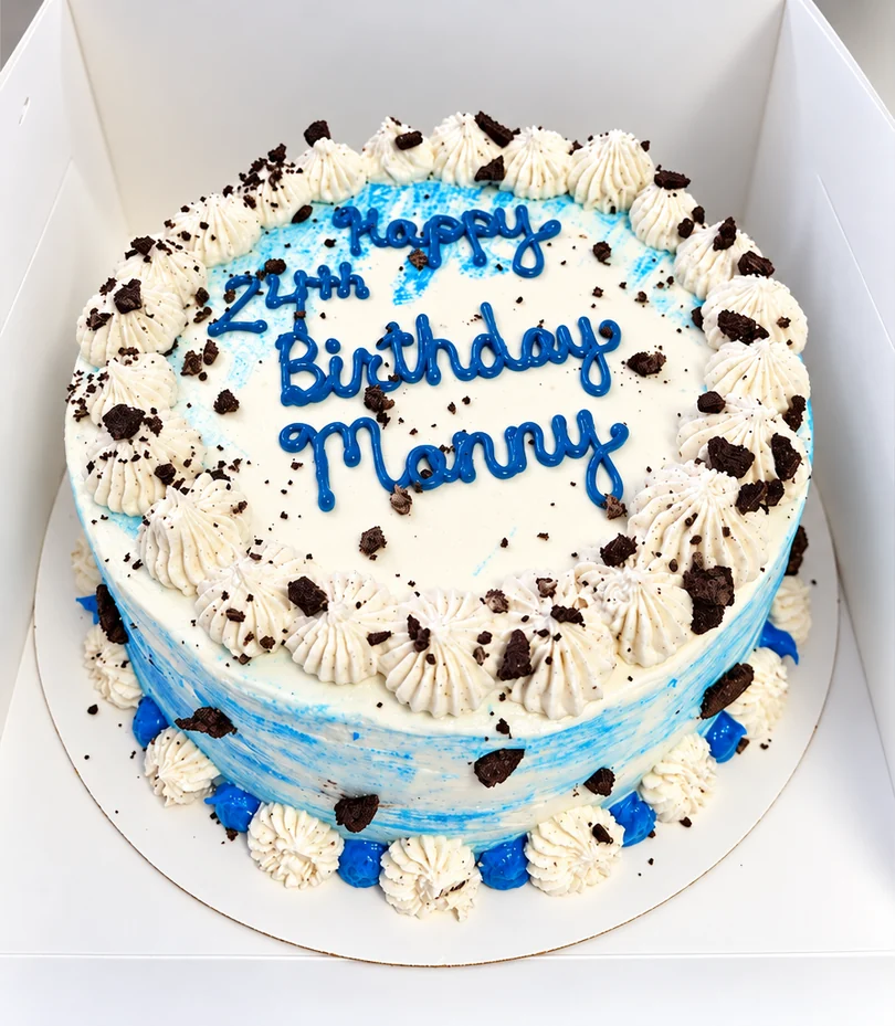 Round birthday cake with blue and white frosting, cookie crumbles and blue piped lettering
