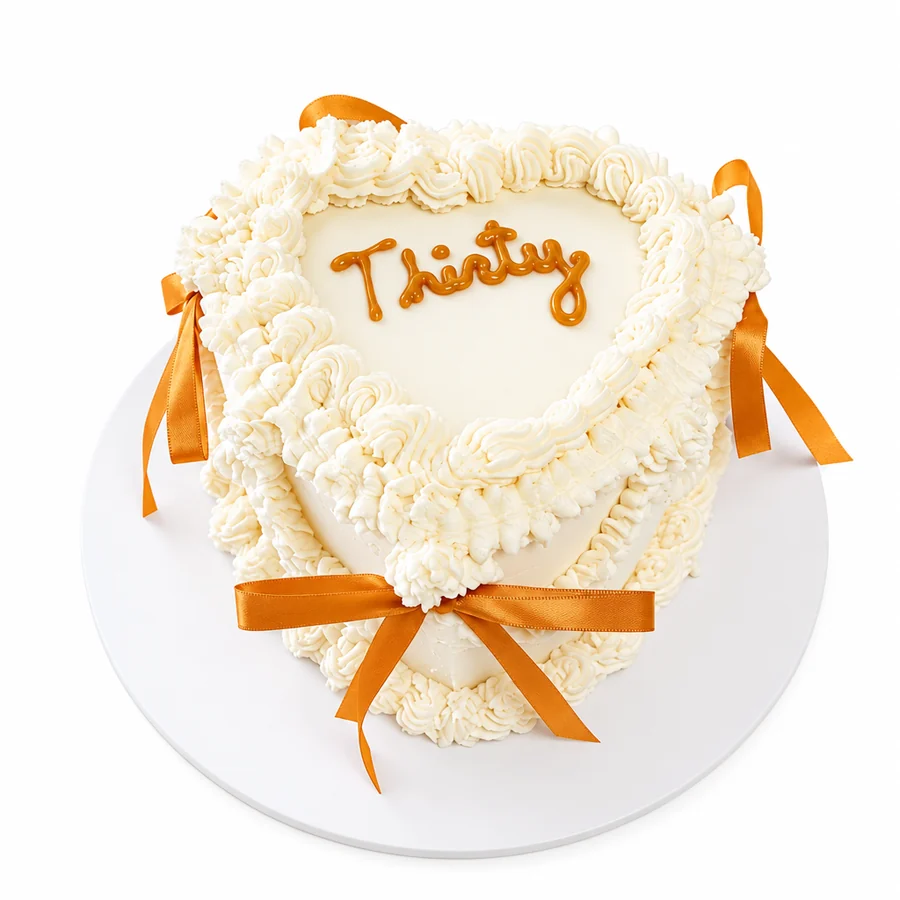 Heart shaped cake with white ruffled frosting, orange ribbons and the word Thirty piped on top