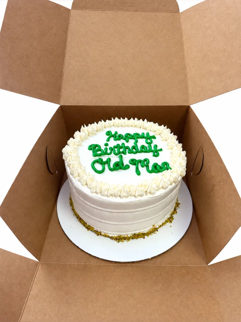 Vegan pistachio birthday cake with white frosting and green lettering in an open box